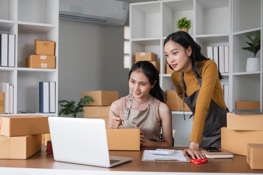 Two businesswomen managing online orders with laptop in office. Concept of e-commerce and teamwork